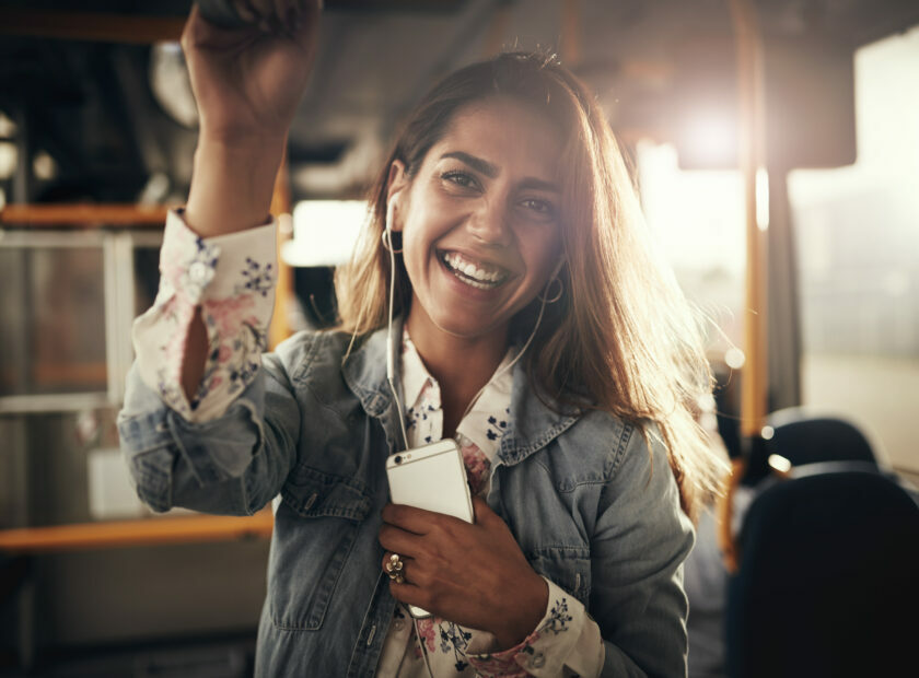 Smiling young woman standing on a bus listening to music