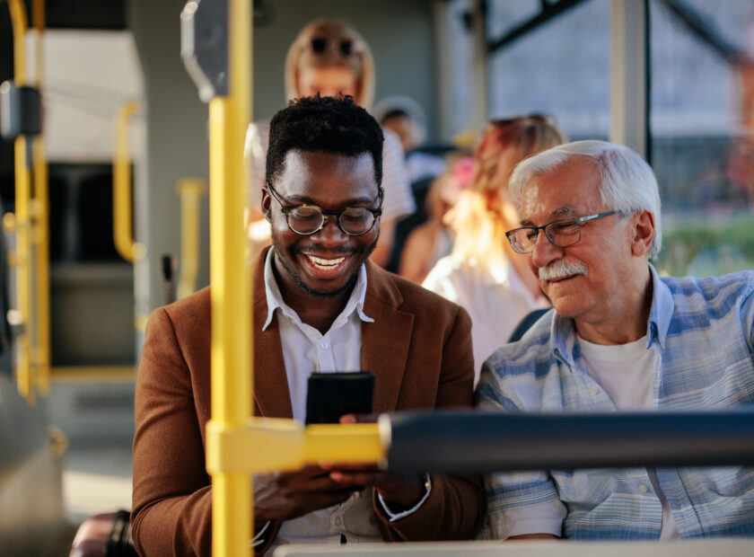 Black man showing senior caucasian man smartphone on public tran