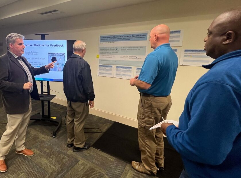 Four men gathered around poster describing strategic goals