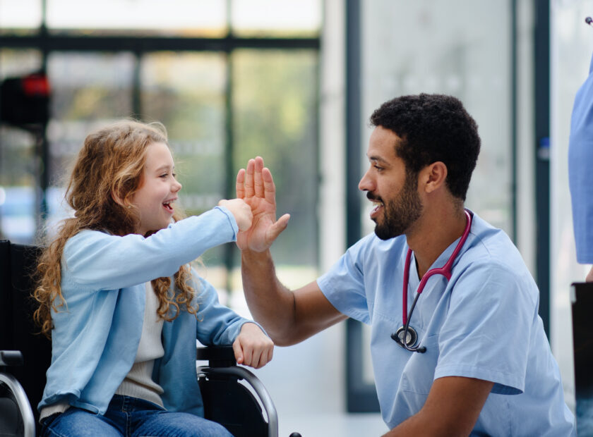 Young multiracial doctor having fun with little girl on wheelchair.